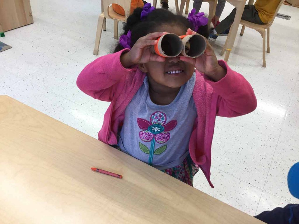 Child looking through a set of binoculars made of paper rolls