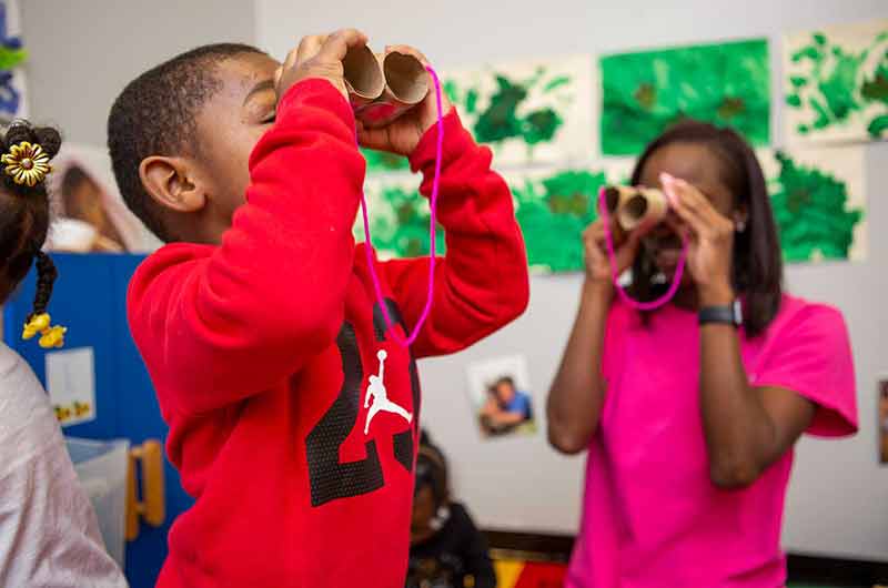 toddler and teacher pretending to look through binoculars