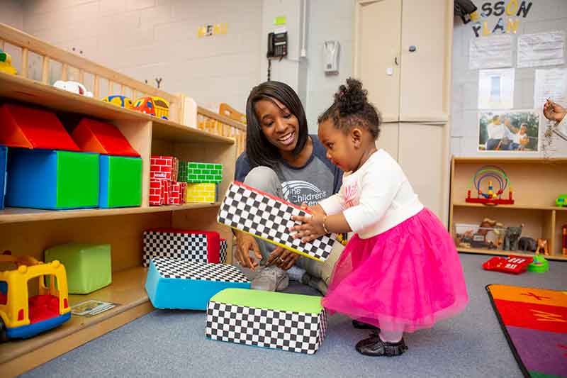 Young toddler stacking blocks with teacher