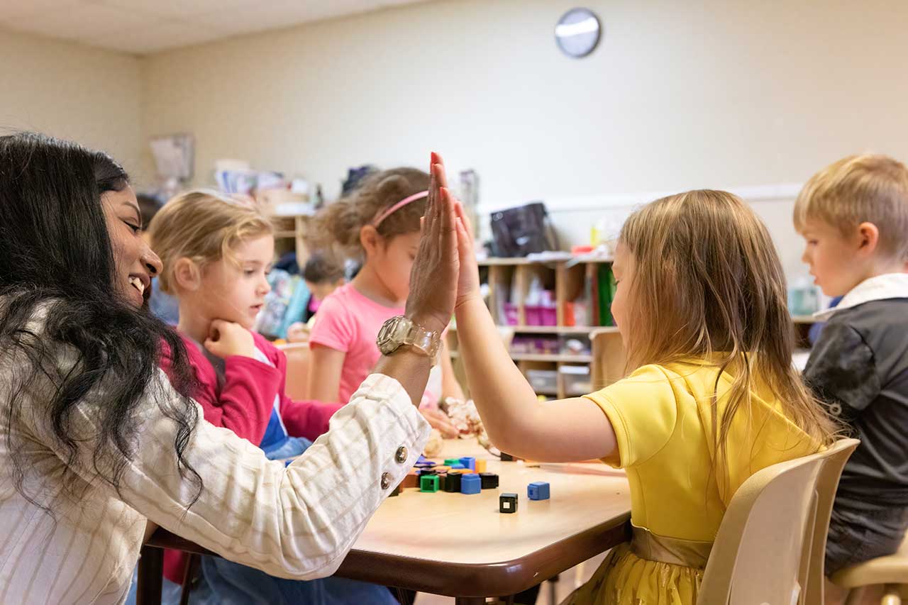 teacher and child giving high five at table