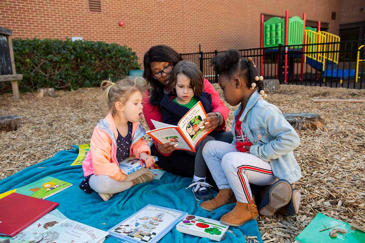 An educator reading a book outside with three preschoolers