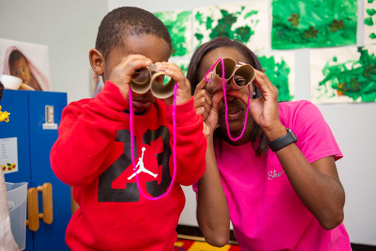 An educator and child holding up pretend binoculars