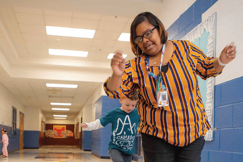 Educator and child walk carefully in a hallway.